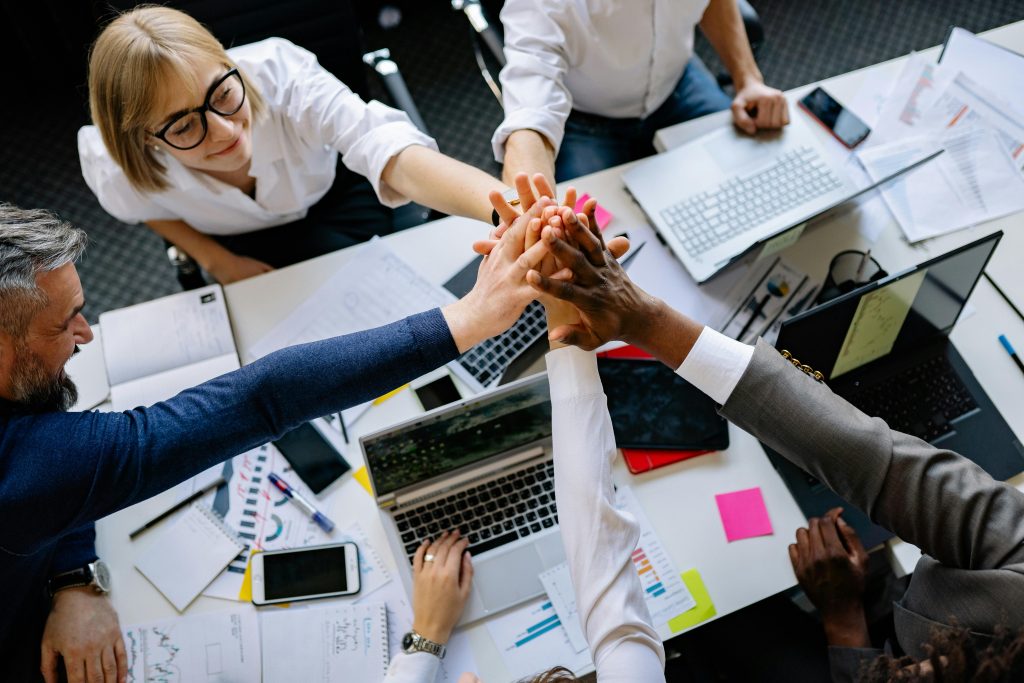 Photo from above of business professionals around a conference table with hands coming together in the center.